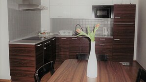 A modern kitchen with dark wood cabinets, a white countertop, a microwave, and a dining area with a wooden table and chairs. - FUKAS Apartments MEDENA (Bratislava)