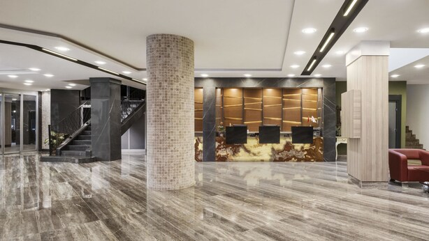 A modern lobby with a marble floor, a central column, a reception desk, and a staircase. - Ramada by Wyndham Mersin (Mersin)
