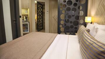 A hotel room with a bed, a minibar, a wall with circular cutouts, and a lamp.