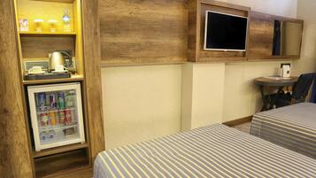 A hotel room with two beds, a minibar, a television, and a small table.