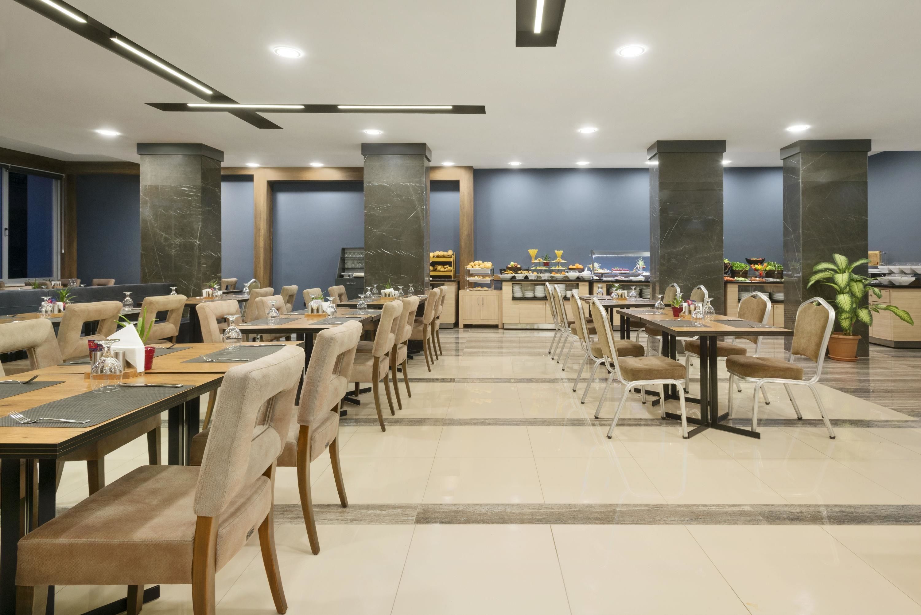 Un comedor amplio con varias mesas y sillas, una barra central con exhibición de alimentos y un diseño de techo moderno.