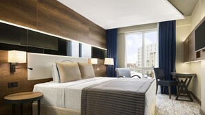 A modern hotel room with a large bed, bedside lamps, a small table, a chair, a TV, and a large window with curtains. - Ramada by Wyndham Mersin (Mersin)