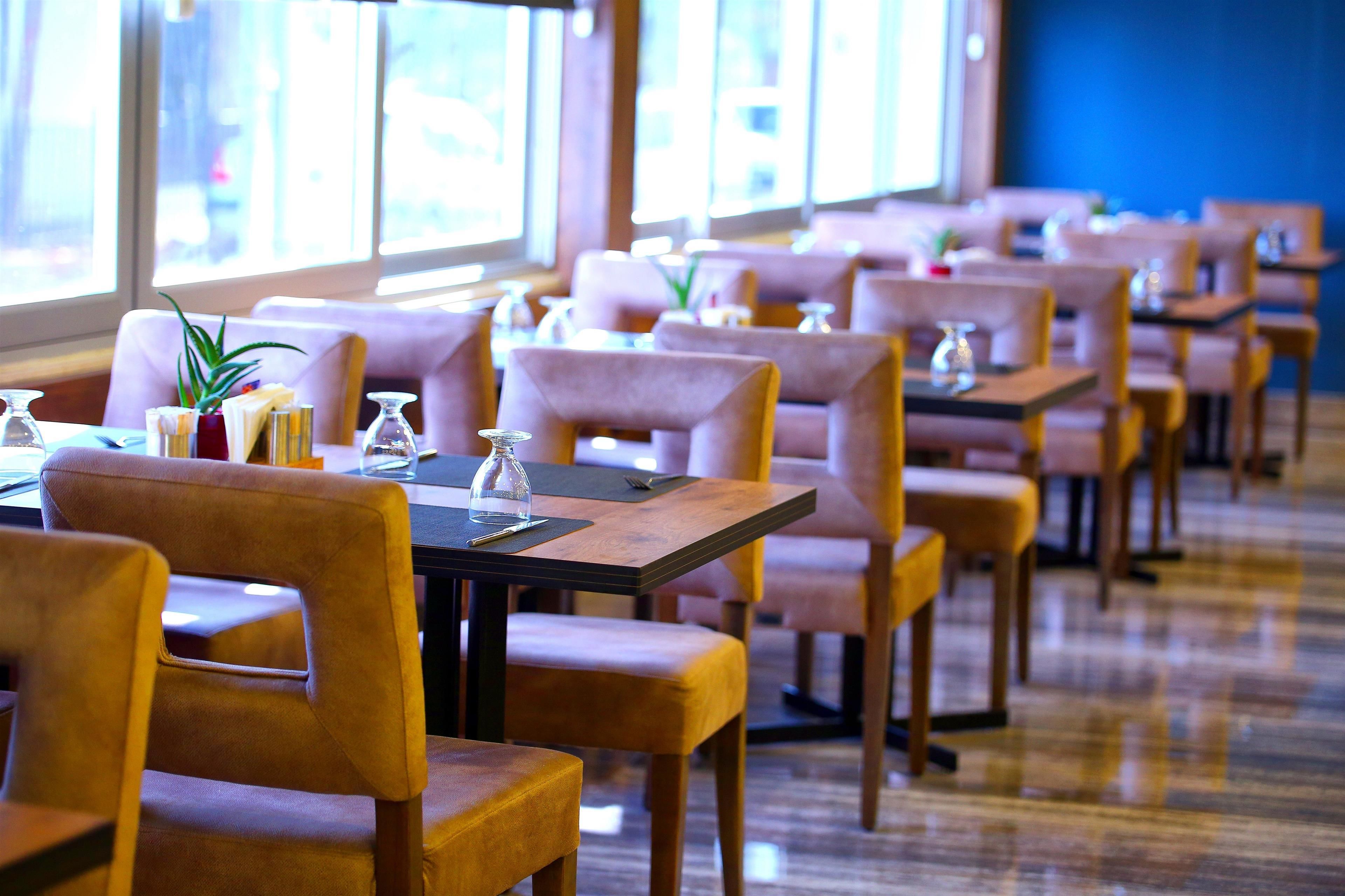 A restaurant with rows of tables and chairs, large windows, and a wooden floor.