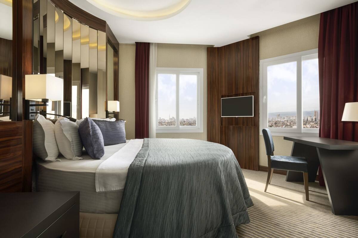 Een hotelkamer met een bed, bureau, stoel, televisie en uitzicht over de stad.