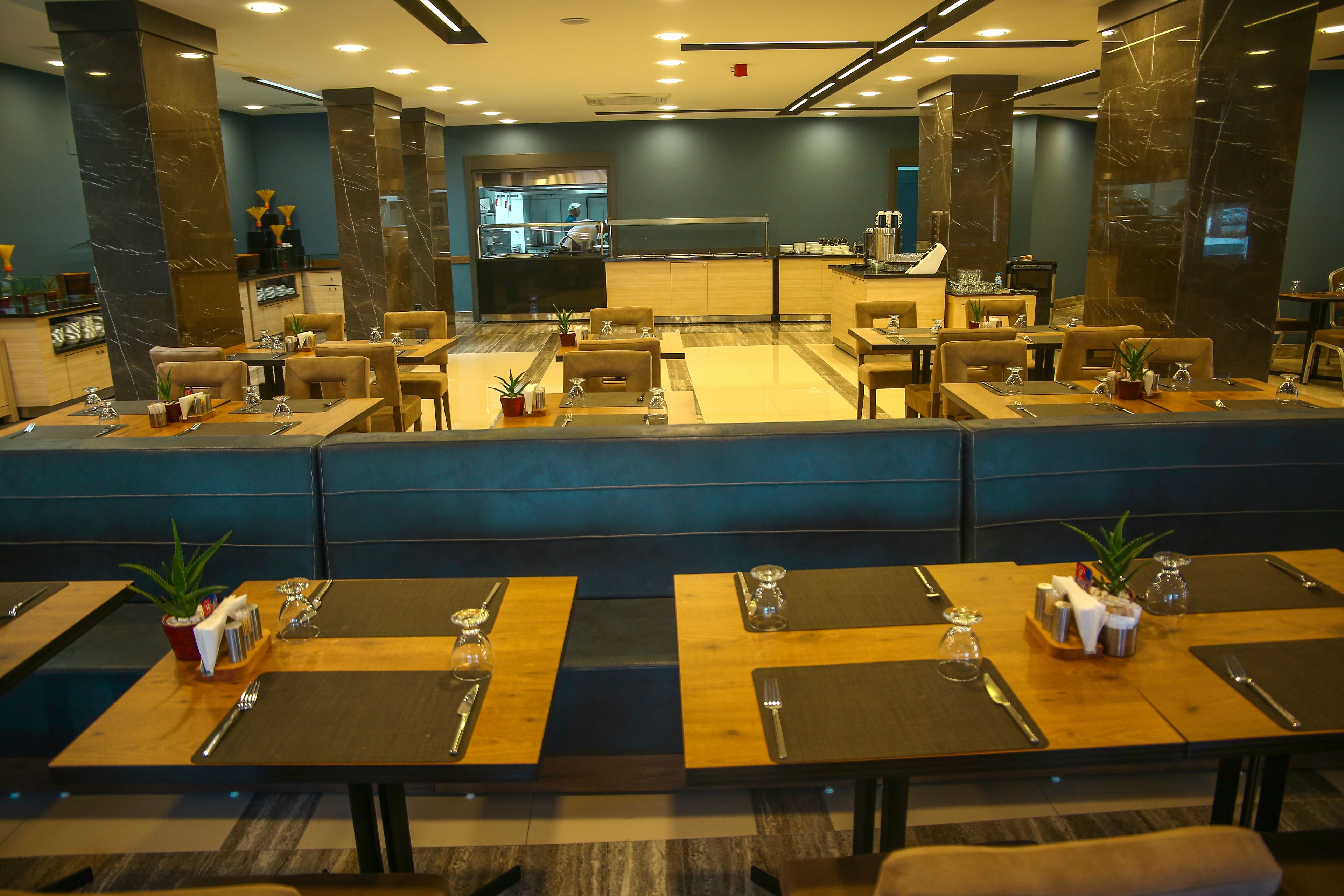 A restaurant with multiple tables, each set with cutlery and napkins, and a kitchen area in the background.