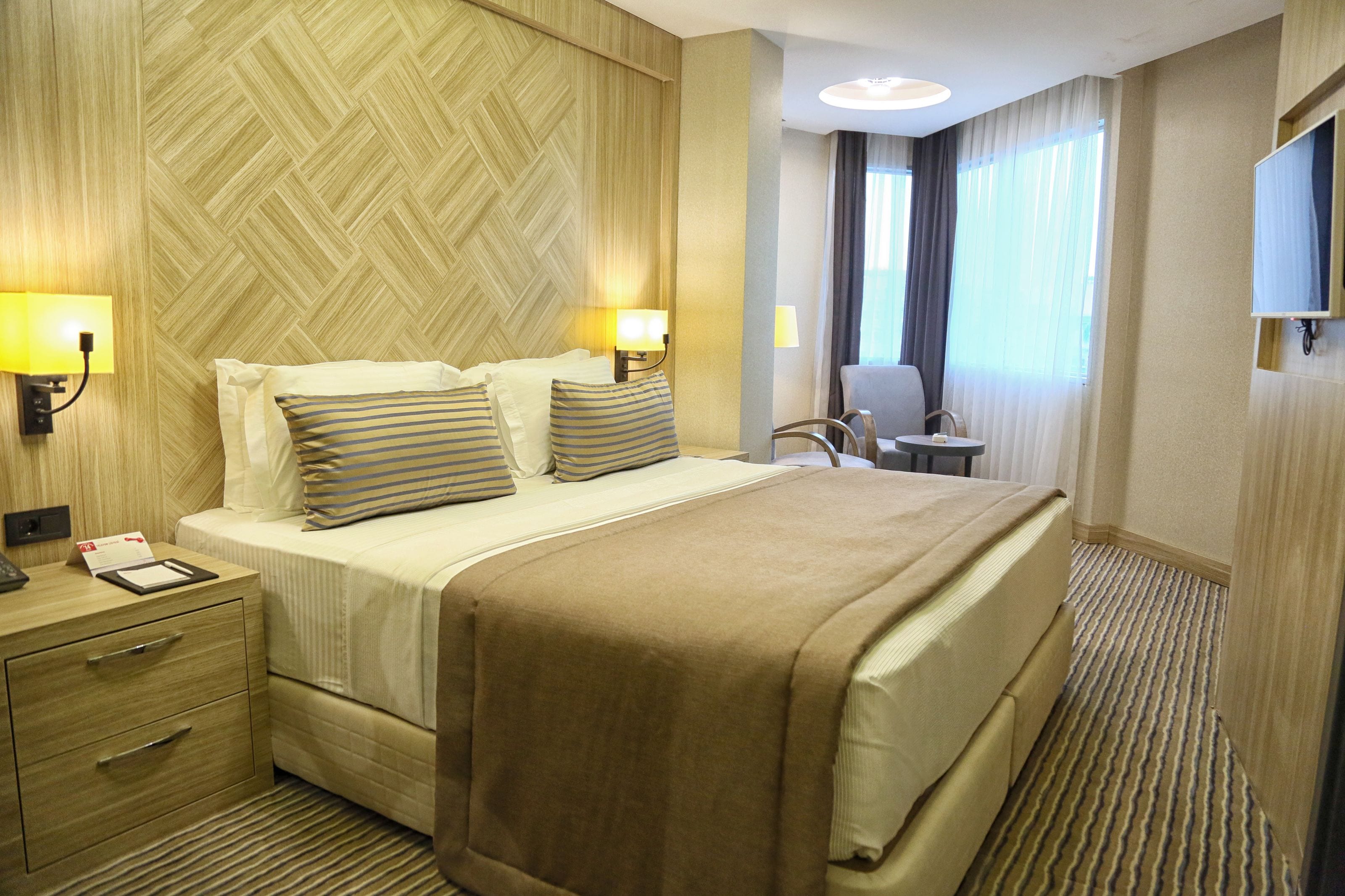 A hotel room with a large bed, two bedside lamps, a desk with a lamp, a chair, and a TV on the wall.