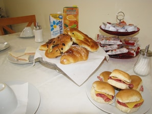Una mesa con diferentes alimentos, entre ellos sándwiches, pasteles y un cartón de jugo.