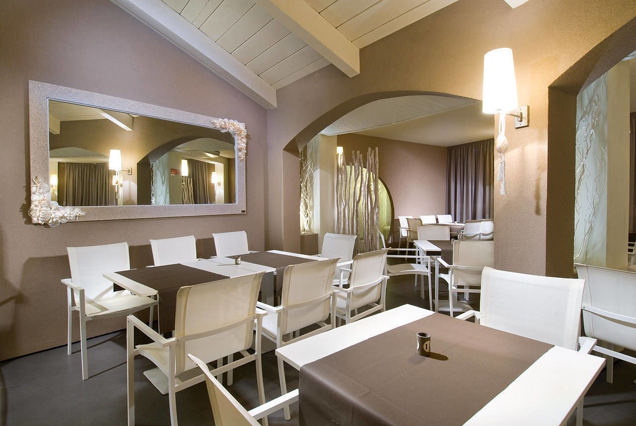Une chambre d’hôtel avec un grand miroir, des chaises blanches, une table à manger et une lampe.