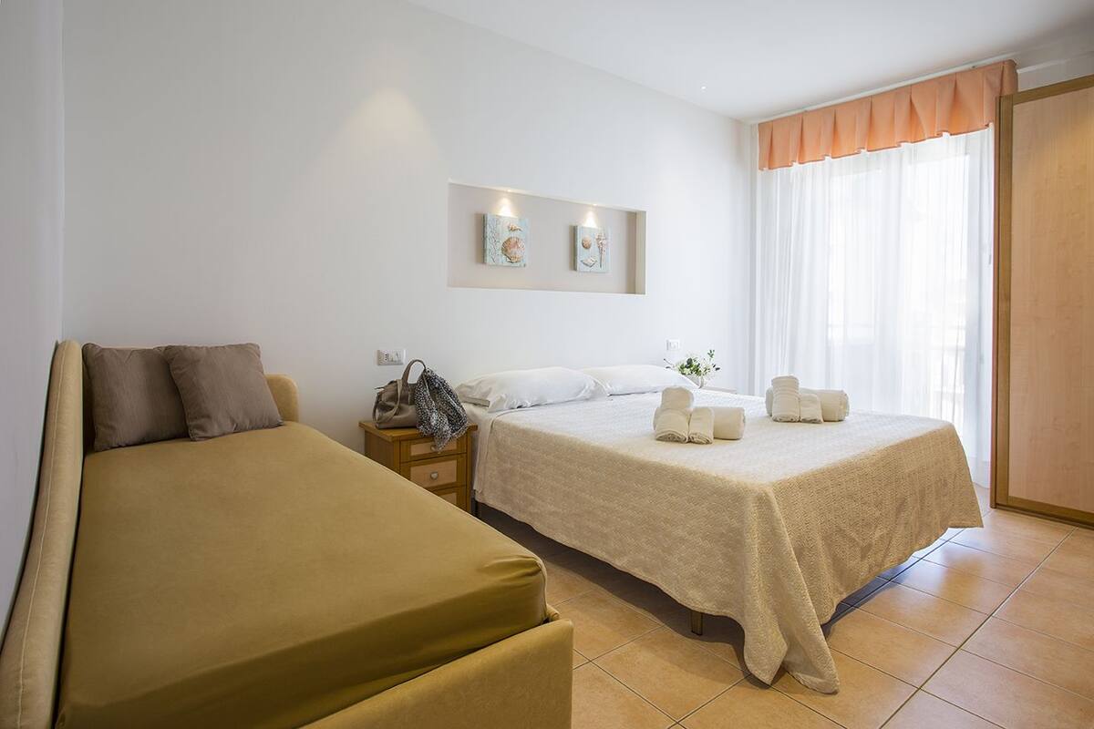 A hotel room with two beds, a small bedside table, a wall-mounted artwork, and a window with curtains.