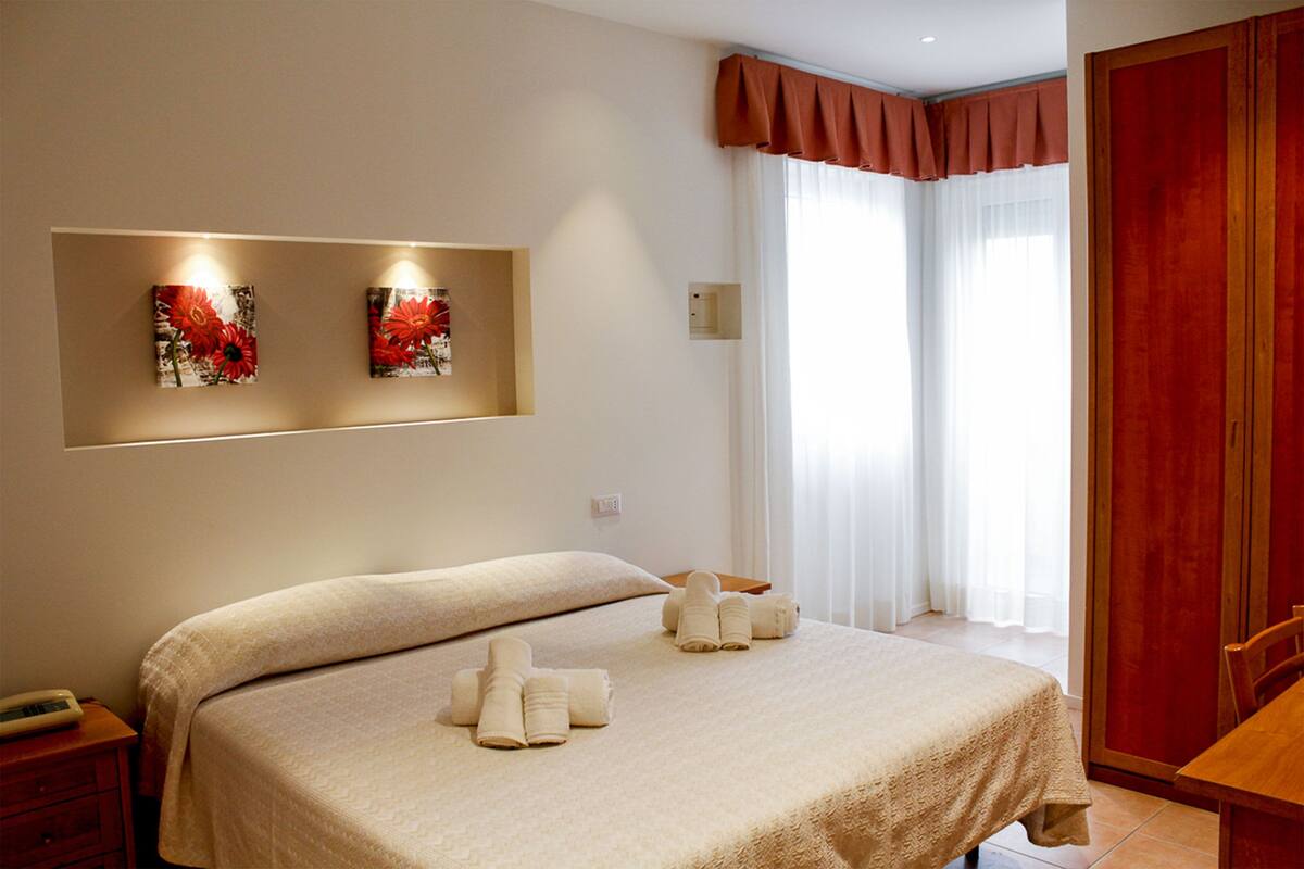 A hotel room with a bed, a nightstand, a wooden table, and two wall-mounted artworks.