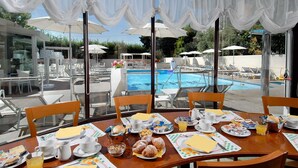 A dining area with a pool view, featuring breakfast setup with plates, cups, and a glass of orange juice.
