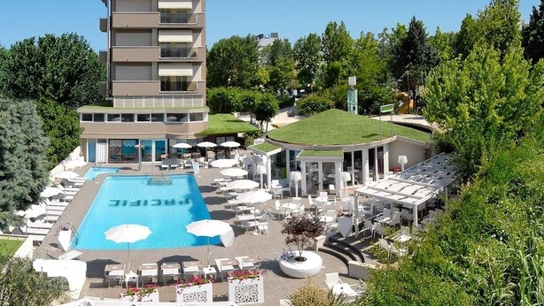 A hotel with a rooftop pool, outdoor seating, and a building with multiple balconies.