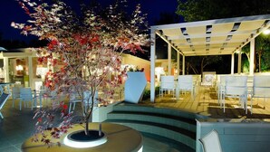 An outdoor seating area with a curved bench, a tree planter, and a covered patio with chairs.