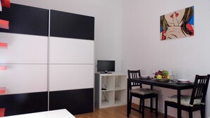 A modern room with a white desk, two chairs, a TV on a stand, and a painting on the wall.