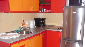 A kitchen with red and orange cabinets, a stainless steel refrigerator, a sink, and a coffee maker.