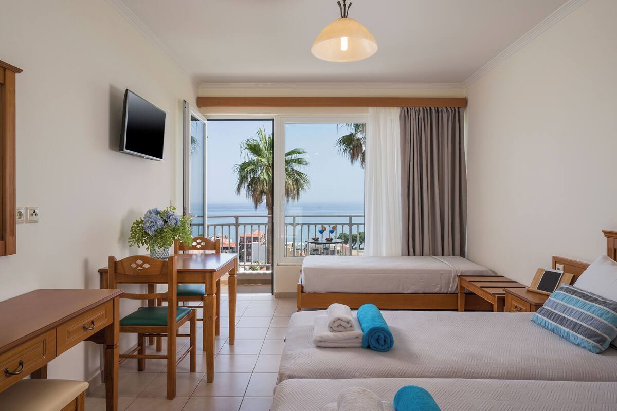 A hotel room with a balcony, a desk, two beds, and a TV.