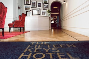 Un hall d’hôtel avec un fauteuil rouge, une moquette bleue ornée du nom de l’hôtel et des tableaux encadrés accrochés au mur.