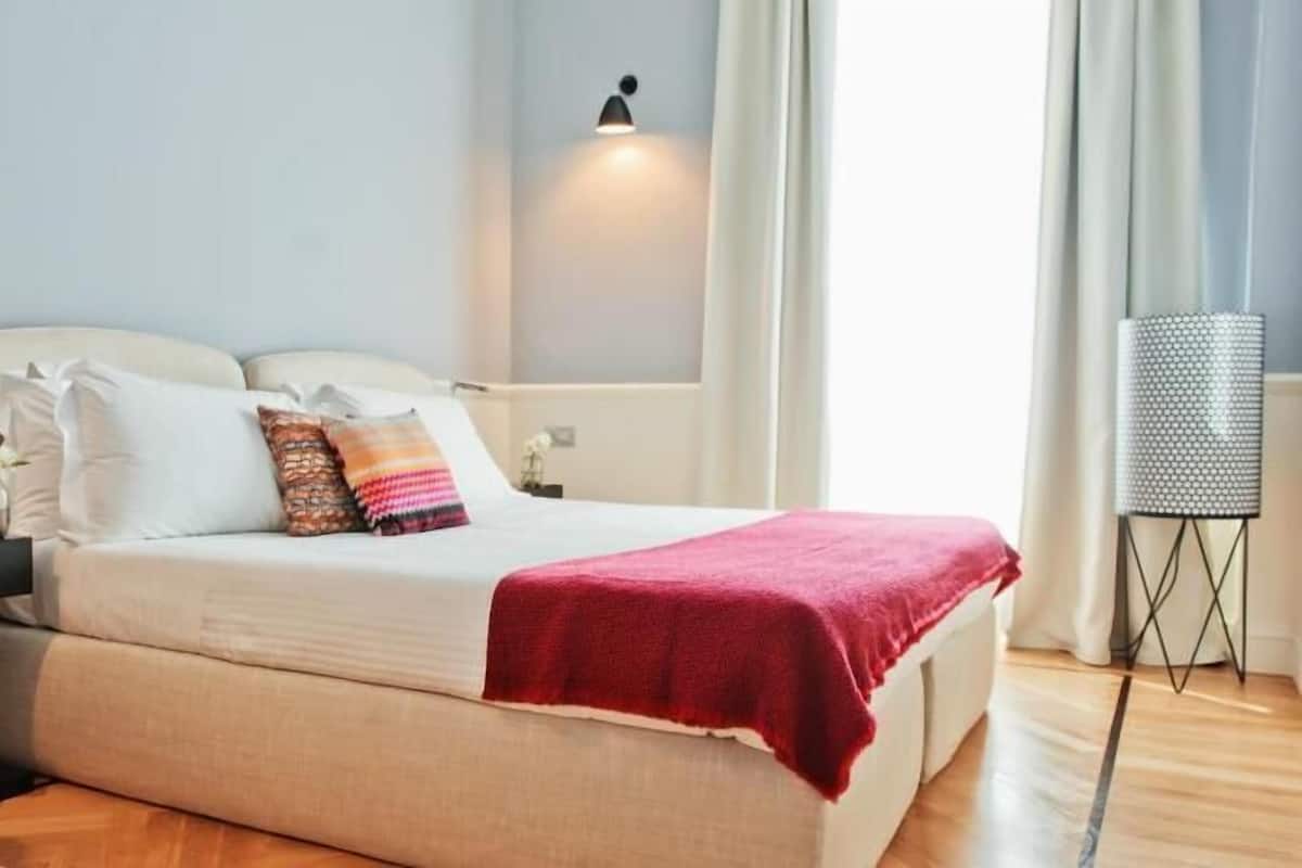 A bedroom with a bed, bedside tables, a chair, a lamp, and a window with curtains.