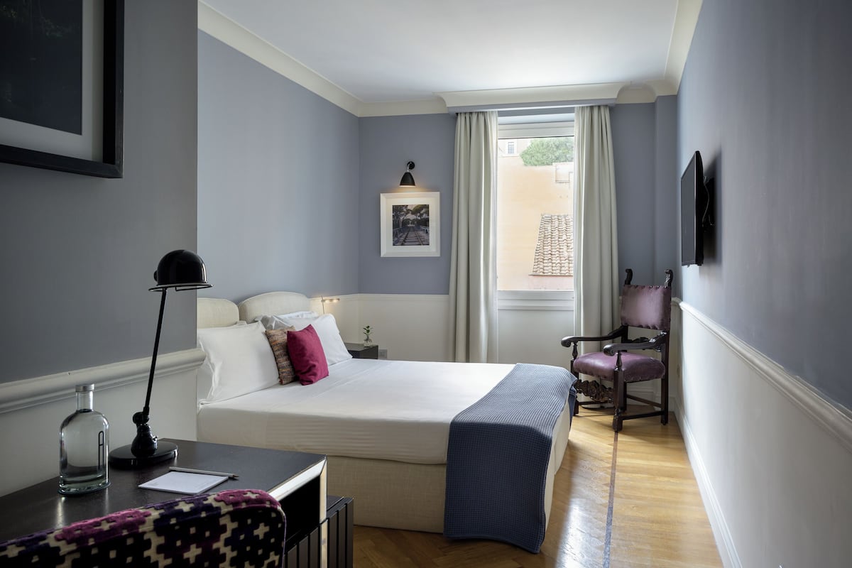 A bedroom with a bed, a desk, a chair, a lamp, and a window with curtains.