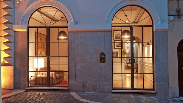 A hotel entrance with two large arched windows, a stone facade, and a well-lit interior visible through the windows. - The Fifteen Keys Hotel (Rome)