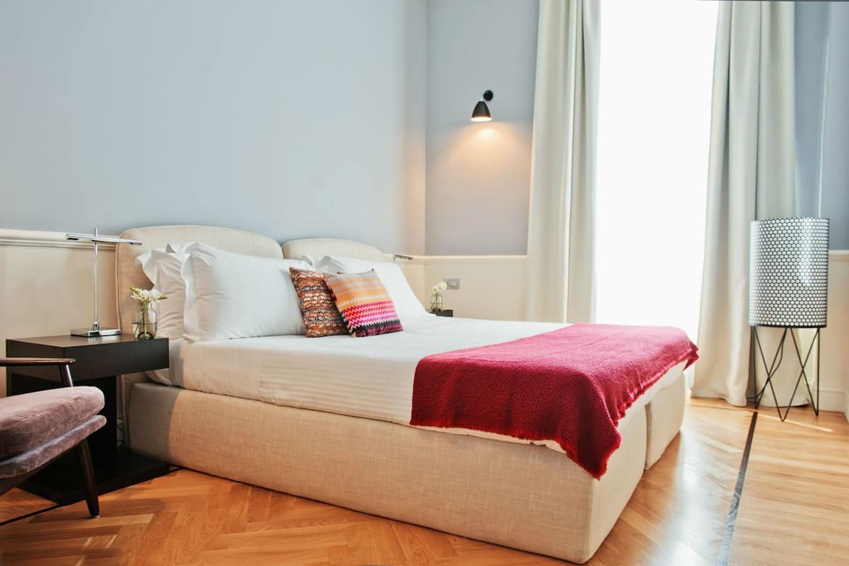 A modern bedroom with a bed, bedside tables, a desk, and a lamp.