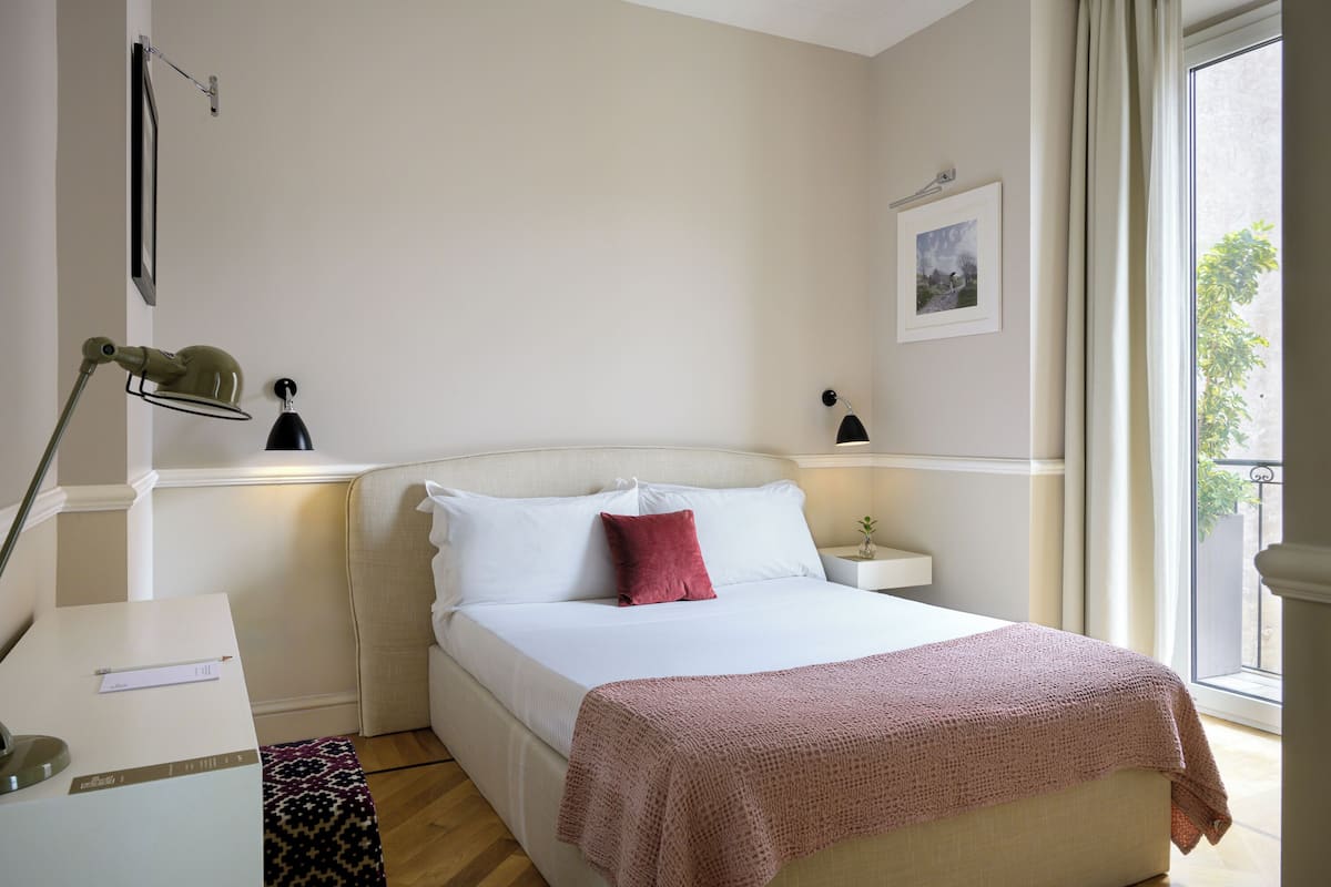 A bedroom with a bed, bedside tables, a desk, a lamp, and a window with a view.