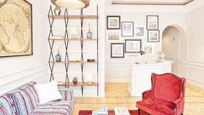 A well-lit living room with a red armchair, a patterned sofa, a wooden bookshelf, and a large map on the wall. - The Fifteen Keys Hotel (Rome)