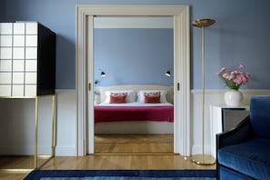 A bedroom with a bed, bedside lamps, a vase with flowers, and a blue chair.