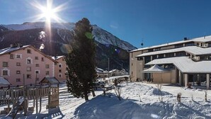 Hotel com paisagem coberta de neve, montanha ao fundo e céu claro.