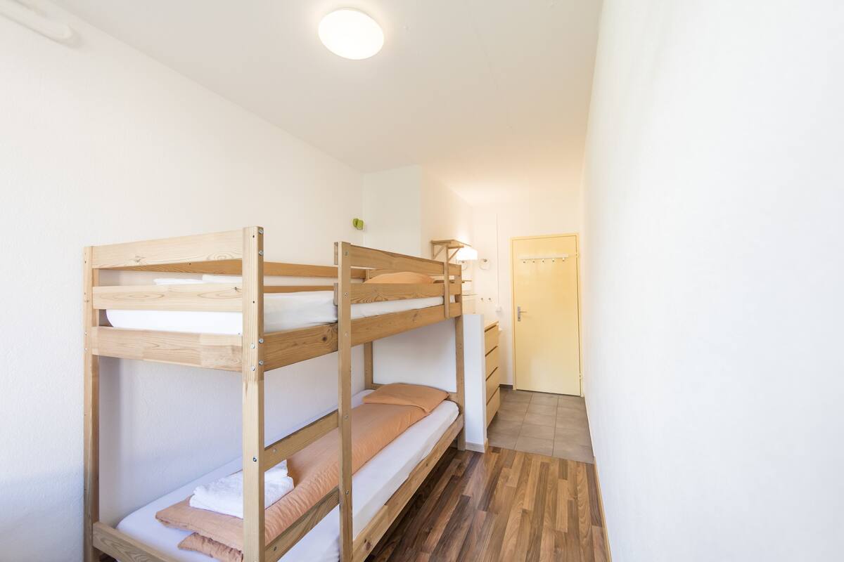 A bunk bed room with a wooden floor and a door in the background.