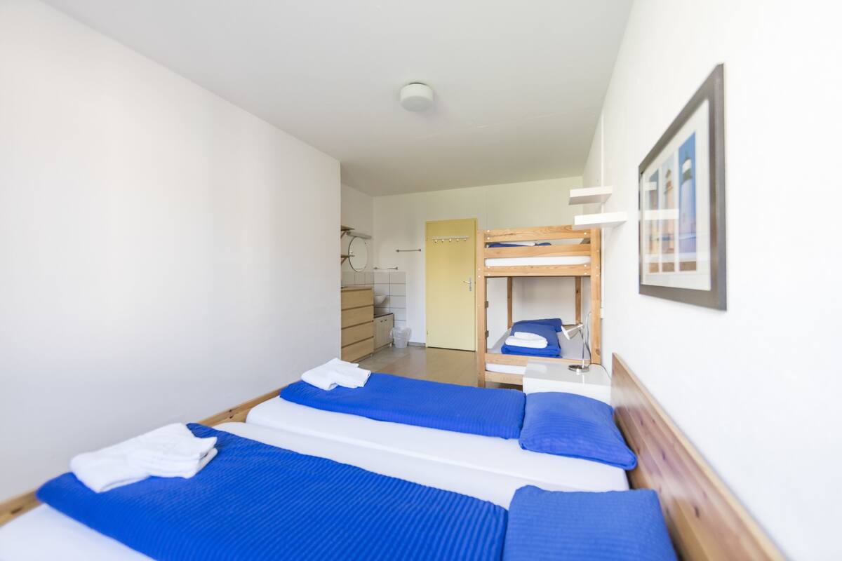 A room with two beds, a wooden bunk bed, a white wall, and a framed picture.