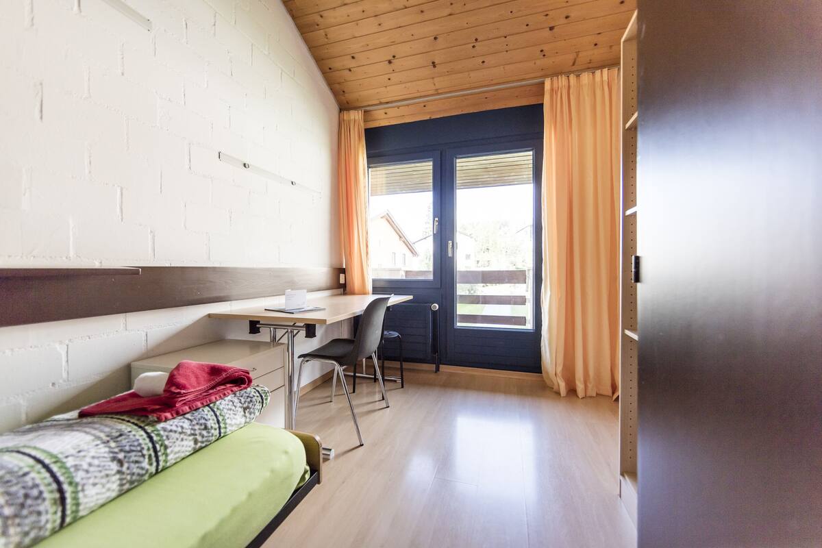 A compact room with a bed, a desk, and a window with curtains.