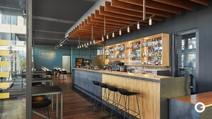 A modern bar with wooden accents, a well-stocked liquor shelf, and a seating area with tables and chairs.
