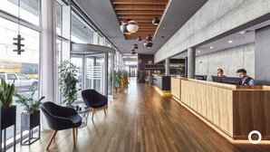 A modern reception area with wooden reception desk, black chairs, and potted plants.