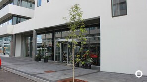 Un edificio moderno con amplios ventanales y un pequeño árbol al frente.