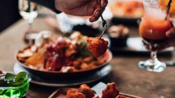 A person holding a fork with food, a glass of drink, and a plate of food on a table.