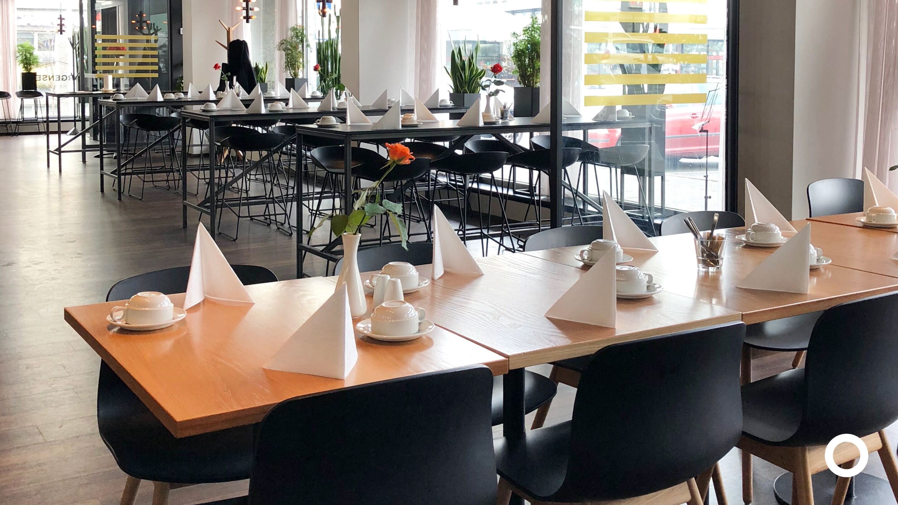 Un restaurant avec de nombreuses tables dressées pour le service, doté de chaises noires et de nappes blanches.