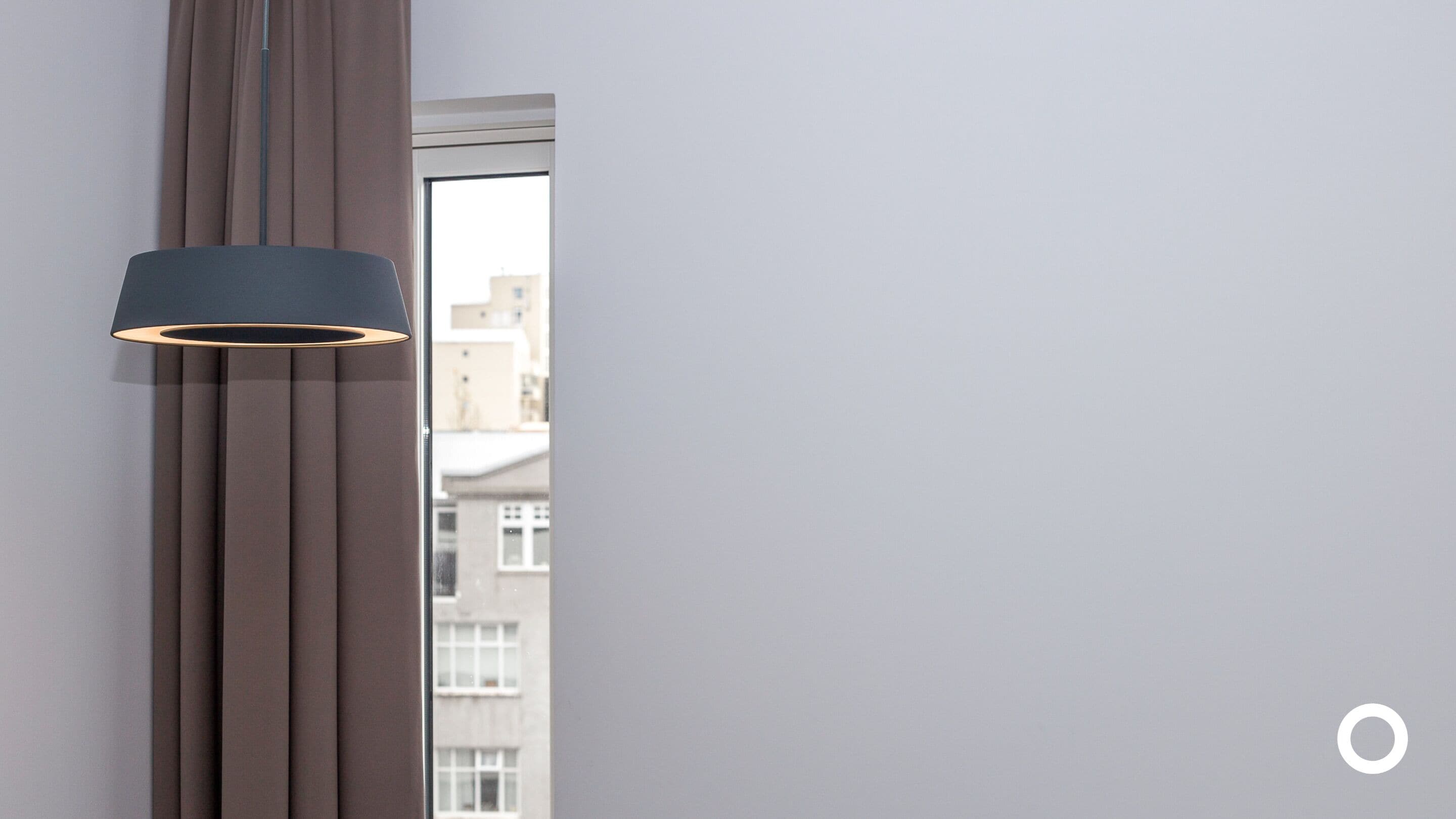 A modern room with a large window, a vertical light fixture, and a view of buildings outside.