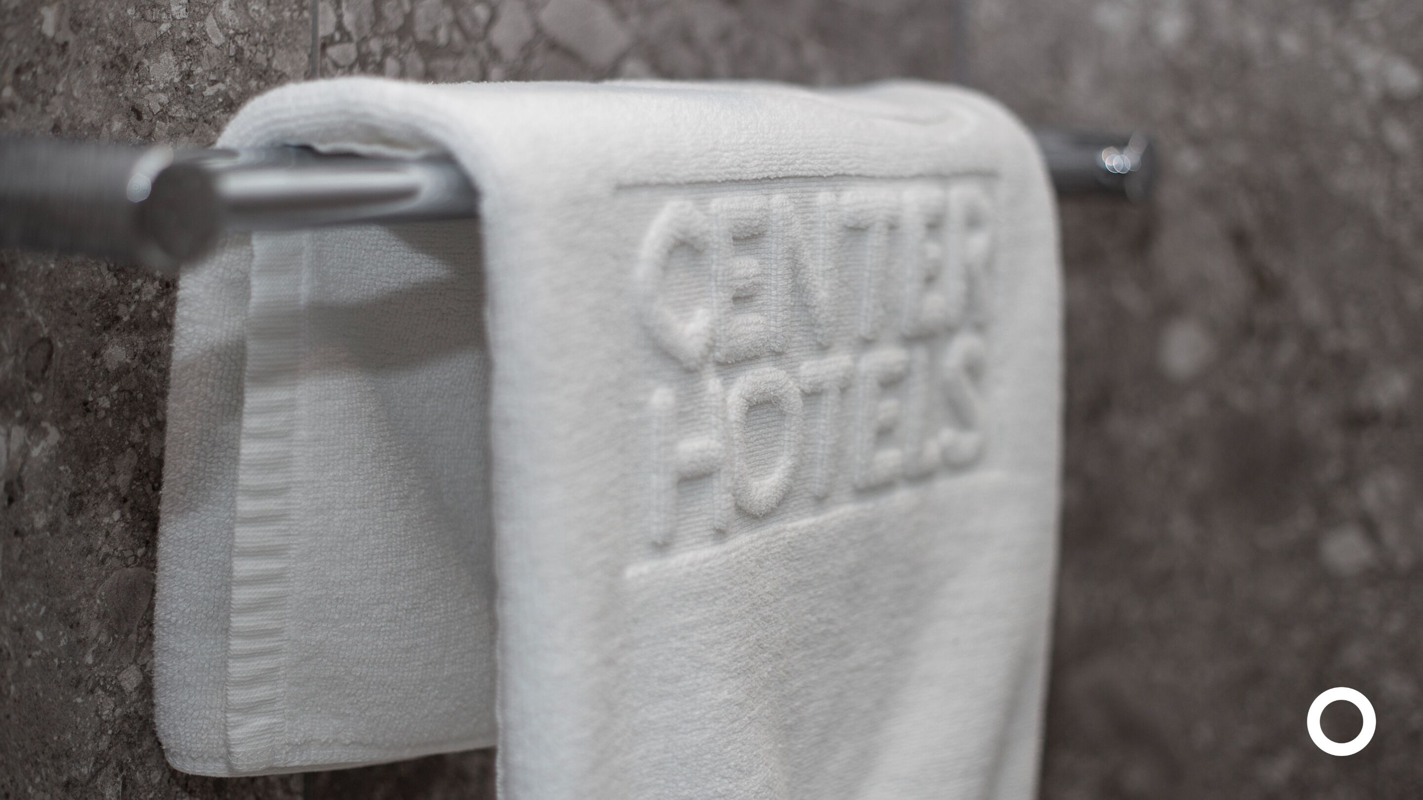 A white towel with "CENTURY HOTELS" embossed on it, hanging on a metal towel bar.
