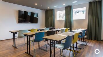 A conference room with tables and chairs, a large screen, and windows with curtains.