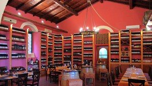 A wine cellar with wooden racks of wine bottles, wooden barrels, and tables set for dining. - Tenuta di Roccadia (Carlentini)