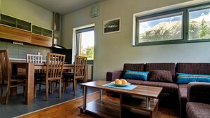 Een moderne woonkamer met een houten eettafel, een bank en uitzicht op bergen door grote ramen.