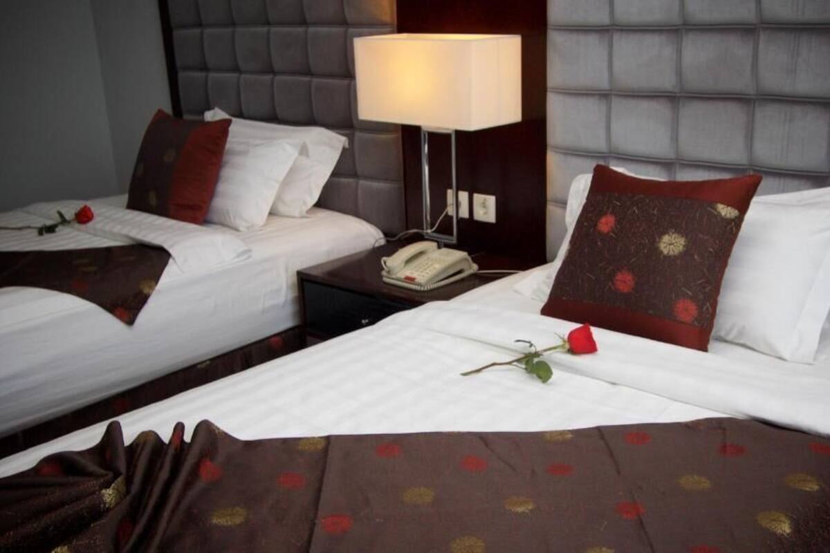 A hotel room with two beds, a bedside table with a lamp, and a telephone.
