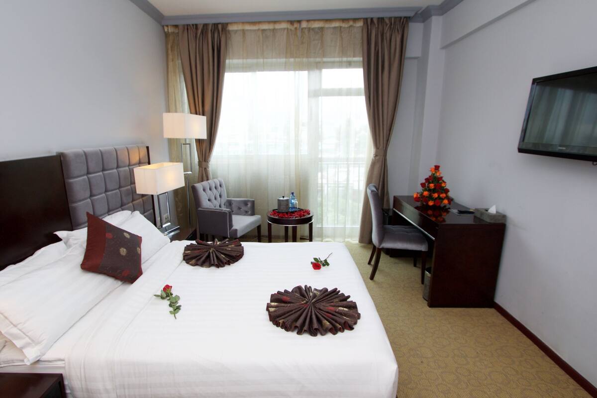 A hotel room with a bed, a desk, a chair, a TV, and a window with curtains.