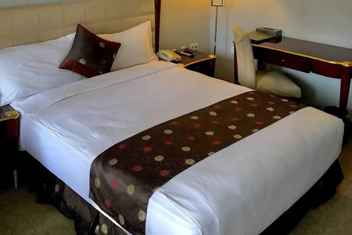 A hotel room with a large bed, a desk, a chair, a lamp, and a telephone.