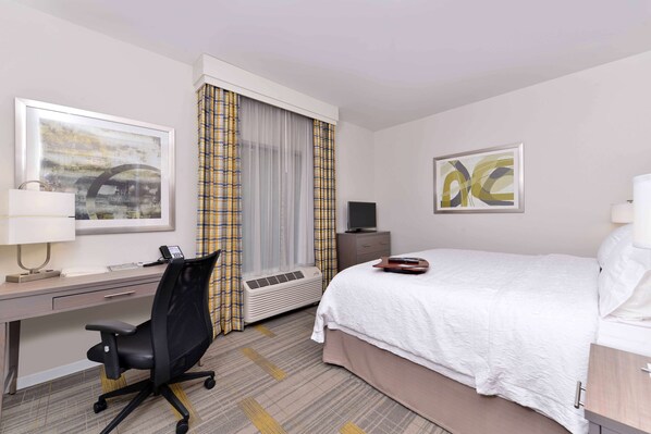 A hotel room with a bed, desk, chair, air conditioning unit, and artwork on the walls.