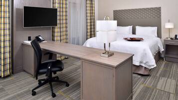 A hotel room with a desk, chair, bed, and a television mounted on the wall.