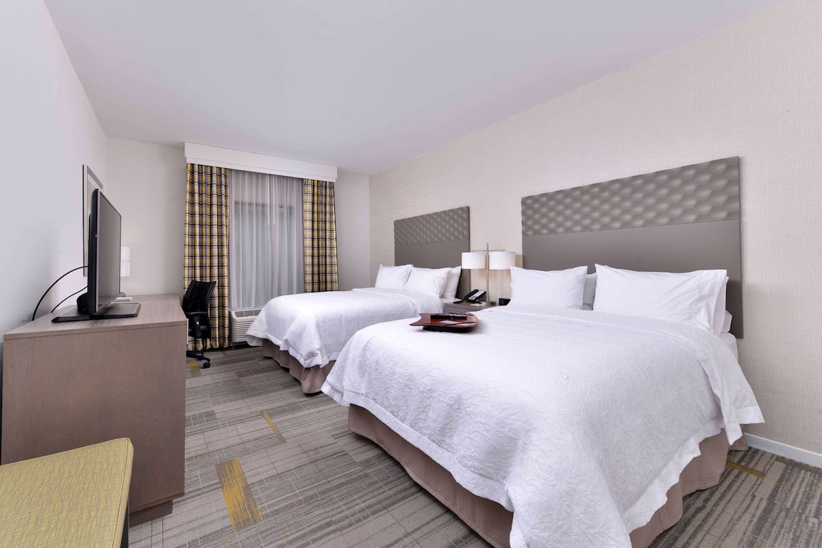 Une chambre d’hôtel avec deux lits, un bureau, une télévision et une fenêtre avec des rideaux.