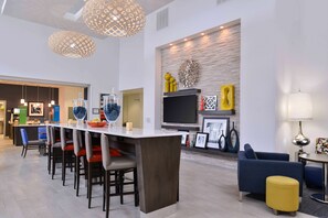 Une cuisine moderne dotée d’un îlot central, de tabourets de bar et d’un coin repas avec un canapé bleu et un pouf jaune.