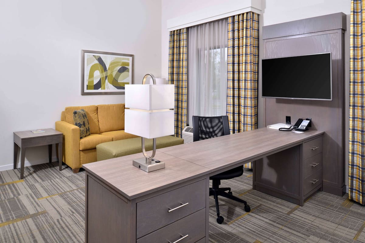 Une chambre d’hôtel équipée d’un bureau, d’un canapé, d’une télévision et d’une fenêtre avec des rideaux.